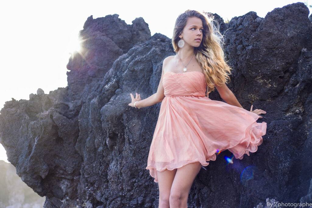 photo de portrait d'une jeune femme avec un robe rose sur un rocher noir