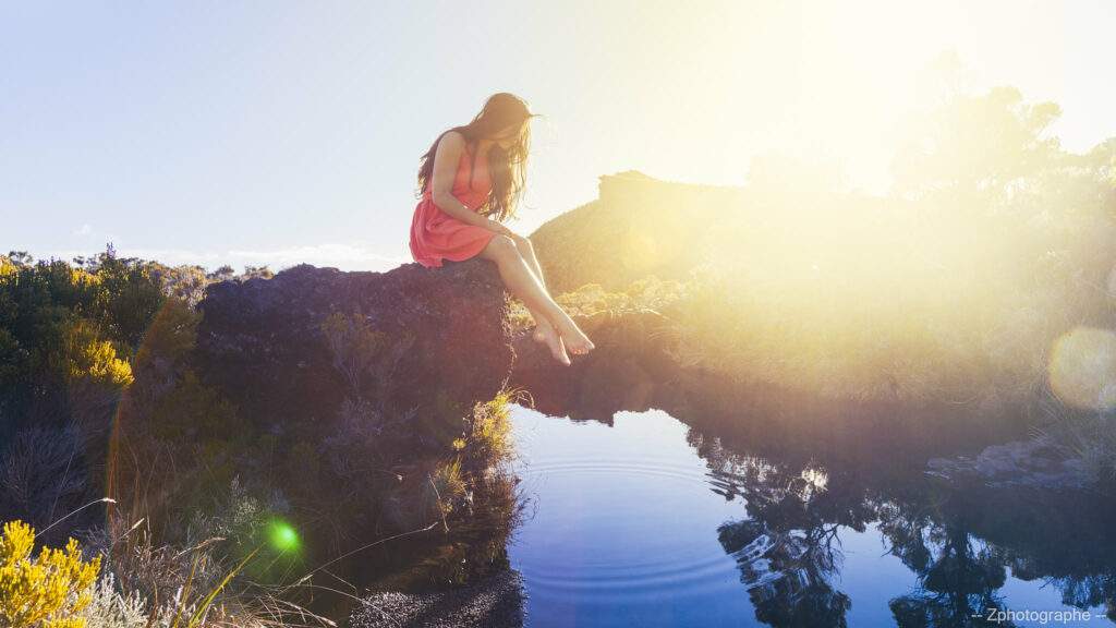 photo d'un paysage avec une jeune femme sur un rochcher et le soleil sur la droite