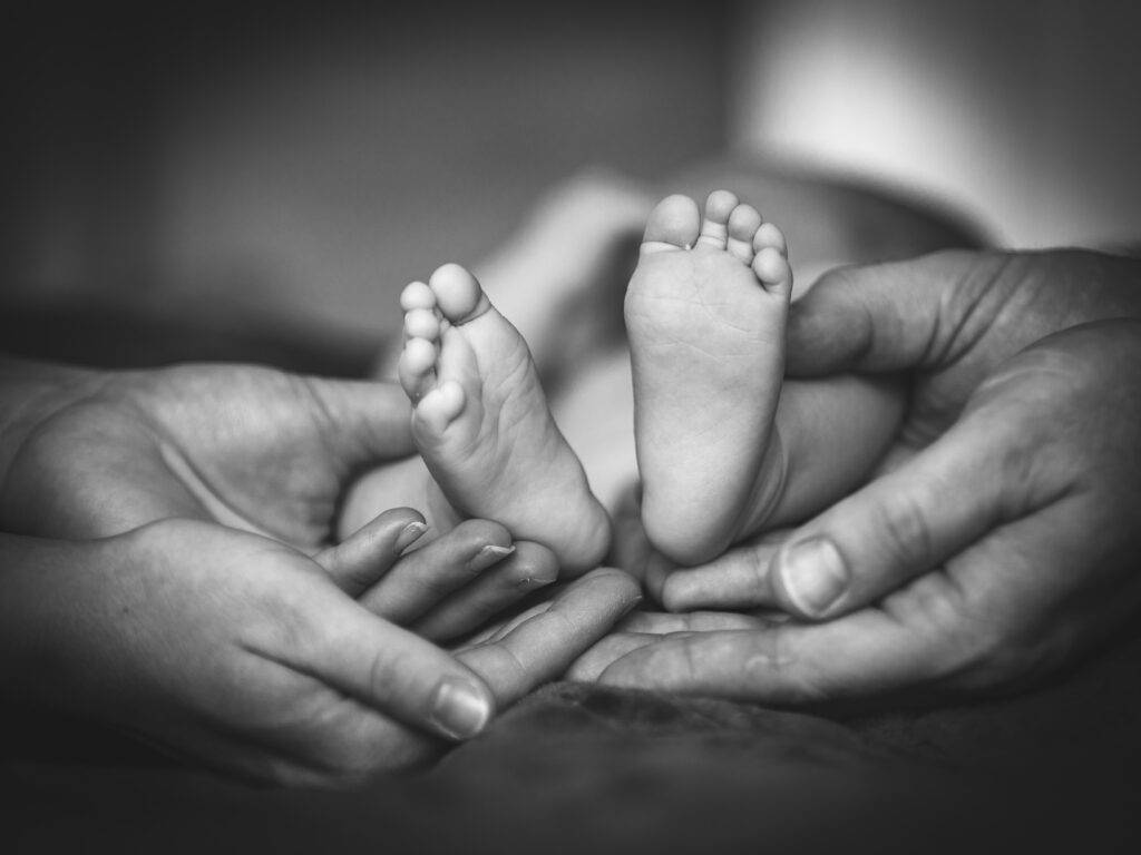 photo de maternité en noir et blanc, les pieds d'un bébé est tenu par les mains des parents