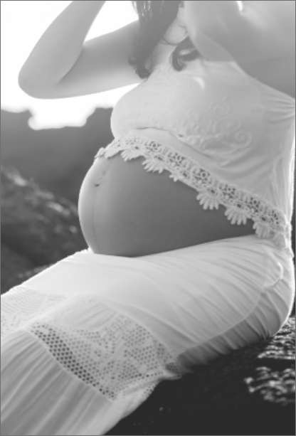 photo en noir et blanc d'une femme enceinte assise sur un rocher volcanique